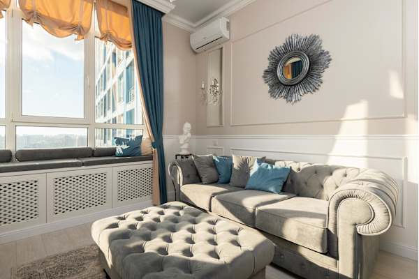 A living room with a grey couch and a round mirror on the wall.